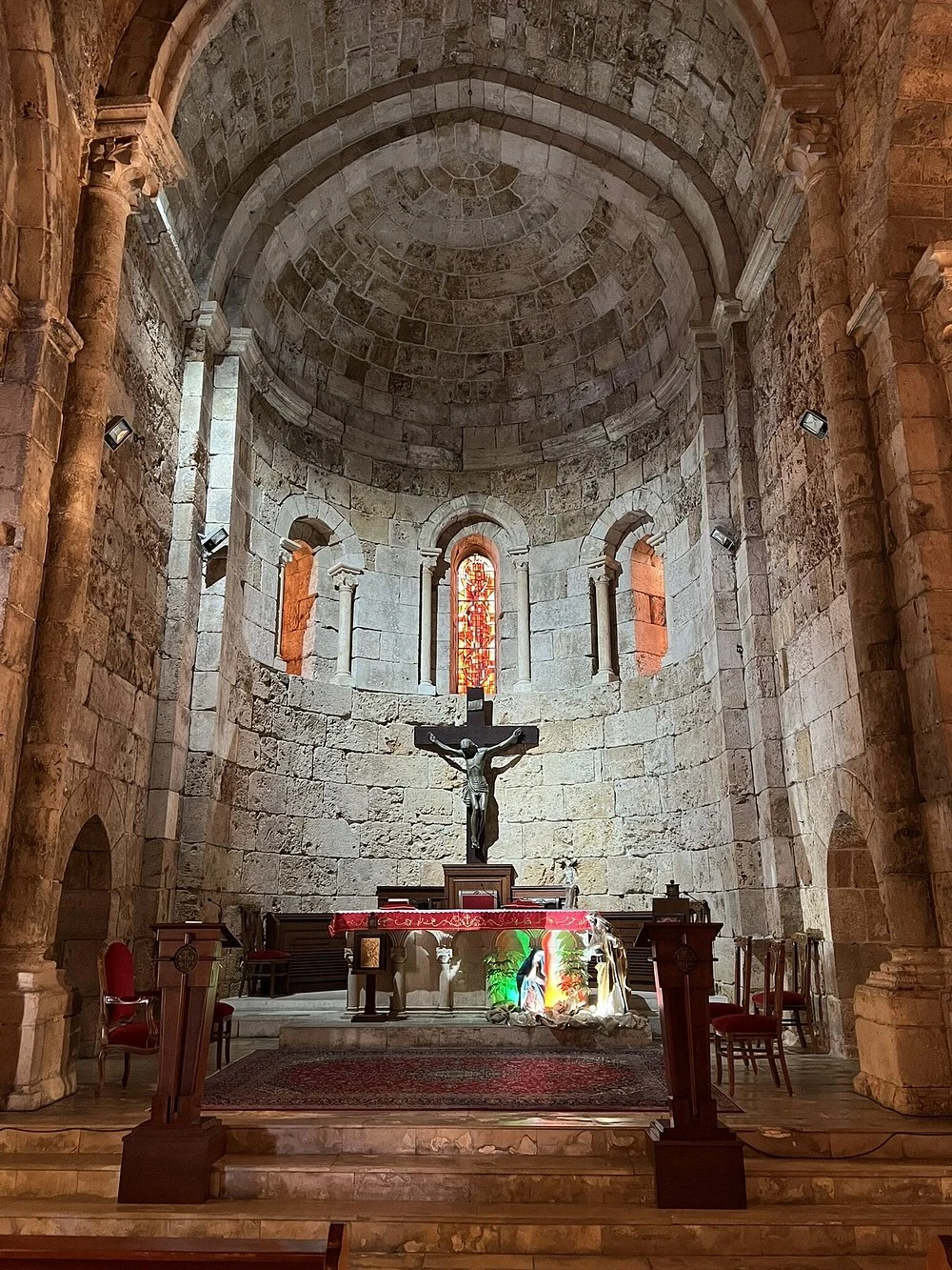 The Romanesque apse of Saint John Mark: stone vault, three arched stained-glass windows and the crucifix above the altar