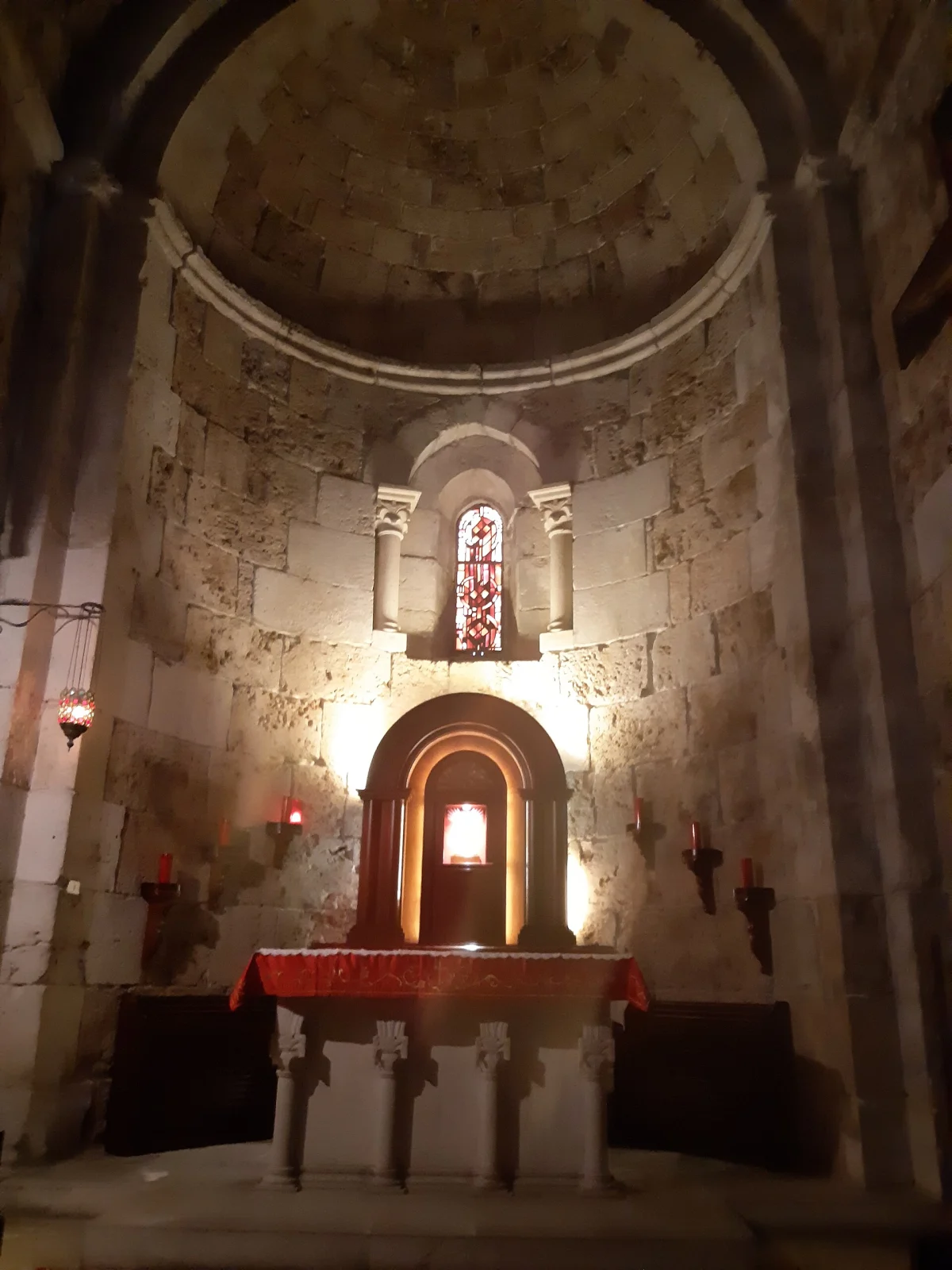 A side altar under a lit stained-glass window in the apse wall