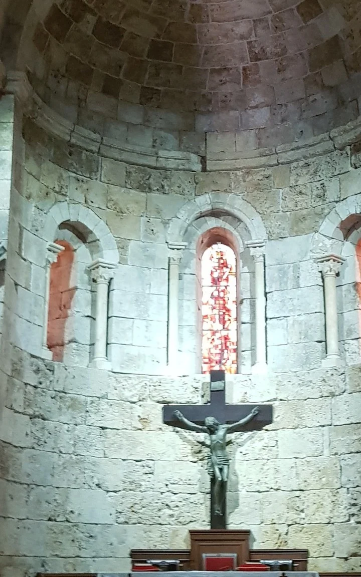 The central window of the apse, its coloured glass glowing above the crucifix