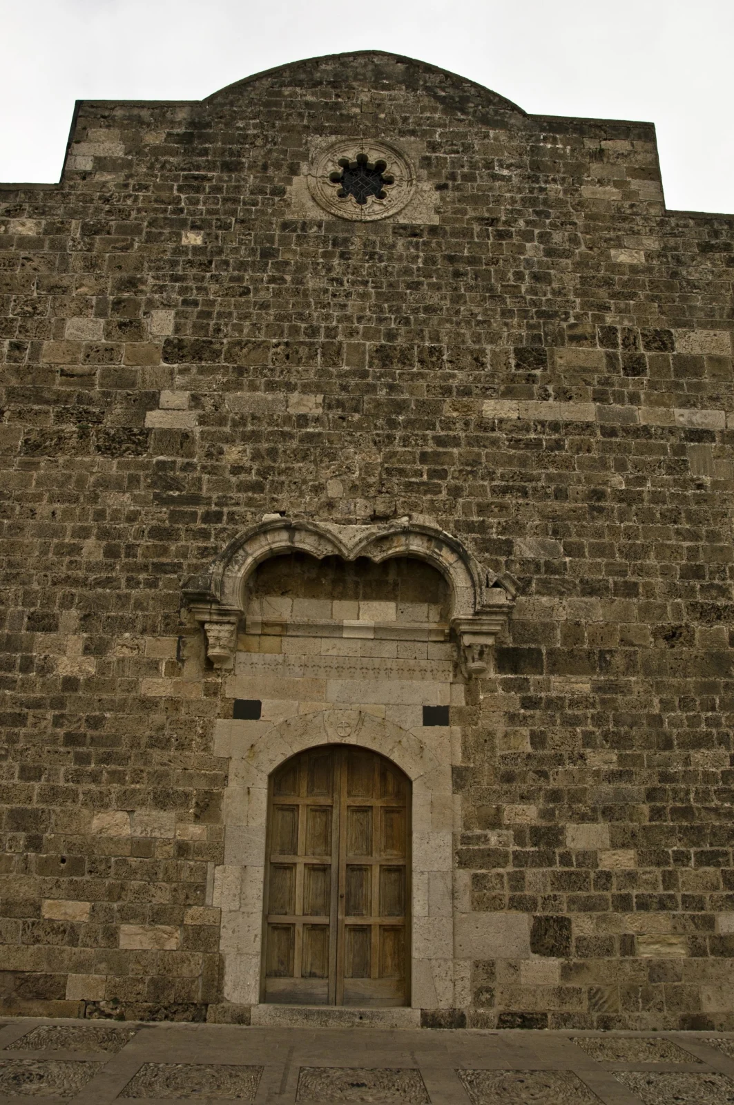 The west facade of Saint John Mark: rough stone, a small star-shaped rose window and a carved doorway
