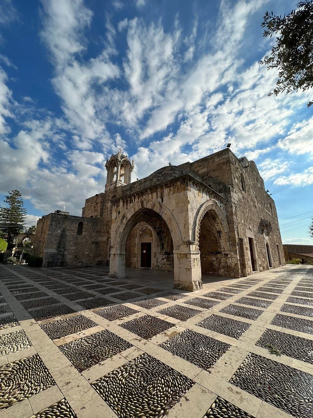 The baptistery and bell tower of Saint John Mark under a sky full of white clouds, over the pebbled courtyard