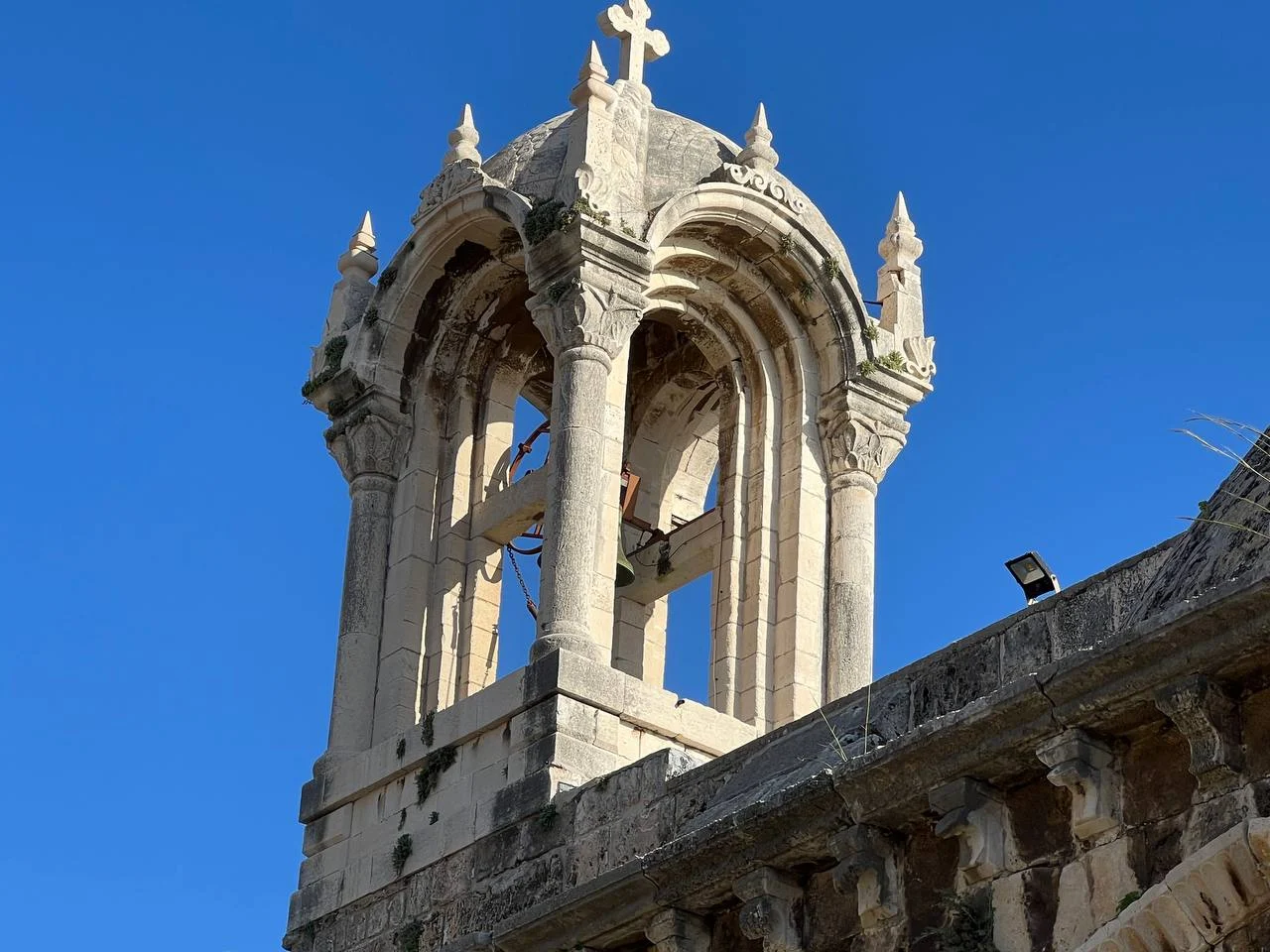 The bell tower of Saint John Mark against a deep blue sky: open arches, carved pinnacles and a stone cross