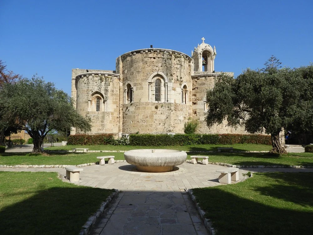 The three apses of Saint John Mark across the garden, with a stone basin, benches and olive trees