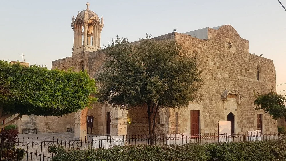 The west facade of Saint John Mark and its bell tower in evening light, behind trees and an iron railing