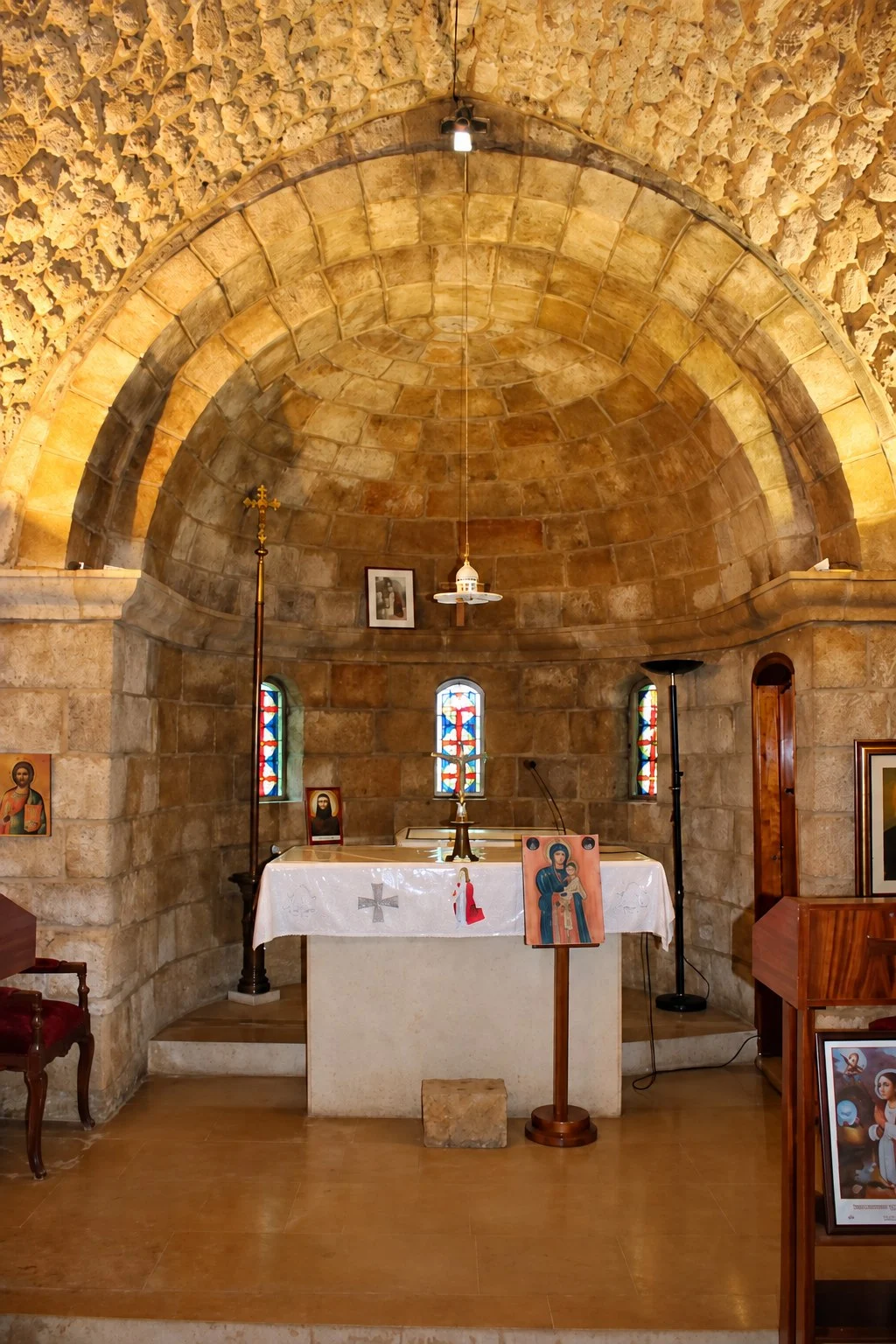 The altar of the shrine of Saint Aquilina under its stone vault, small coloured windows behind