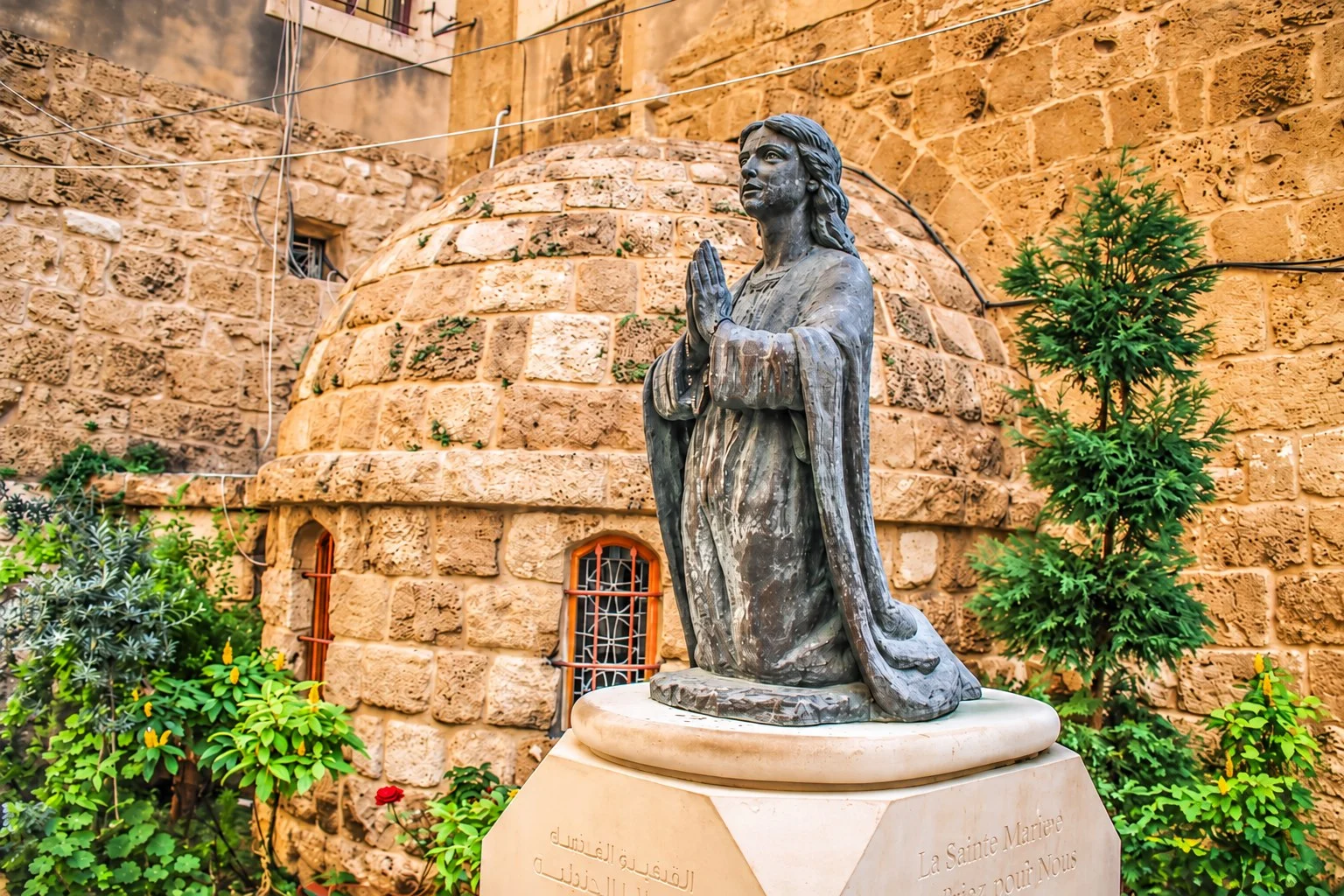 A bronze statue of Saint Aquilina kneeling in prayer before the domed stone shrine