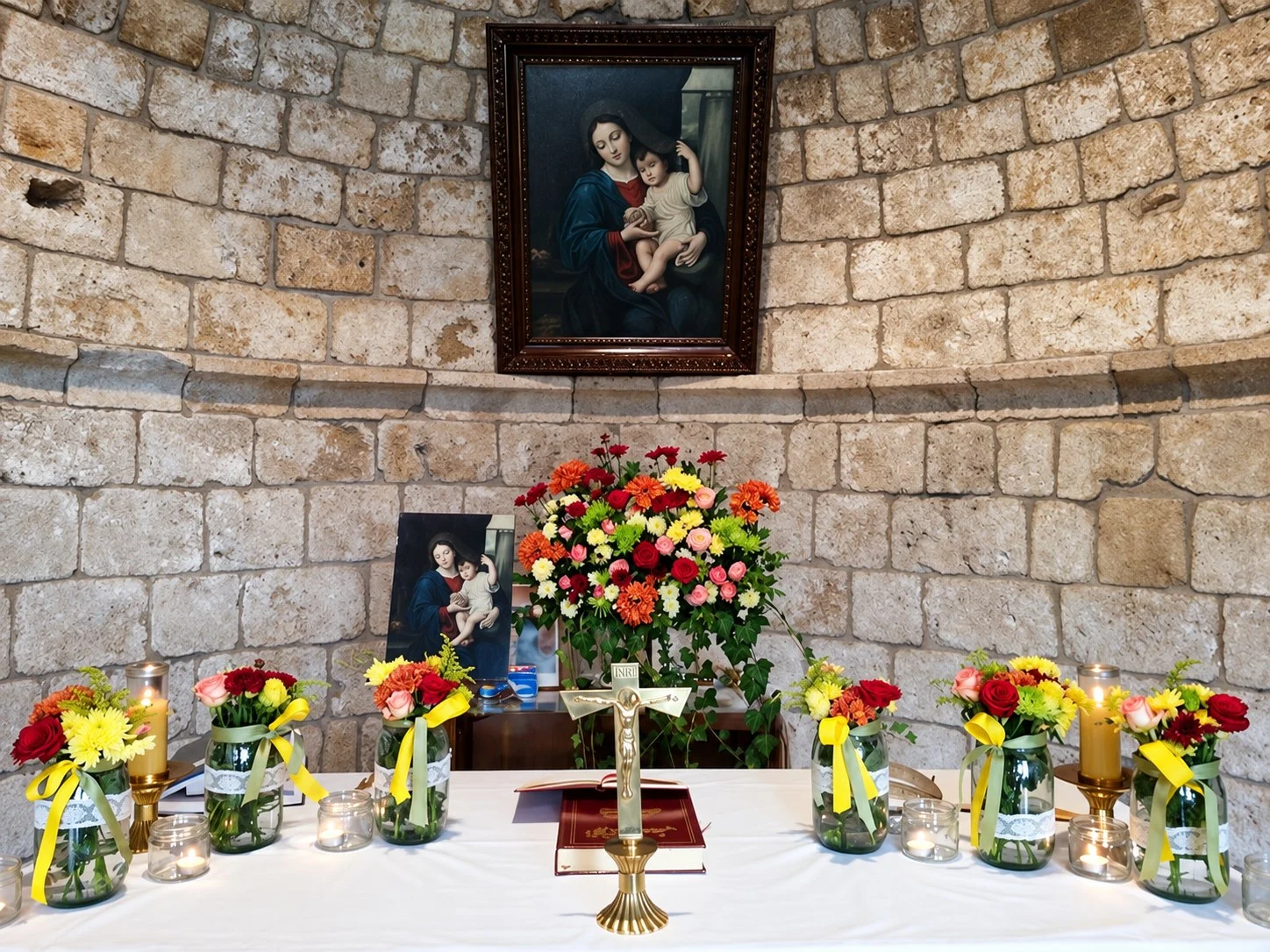 The oil painting of the Virgin holding the Divine Child above the altar, set with flowers and candles