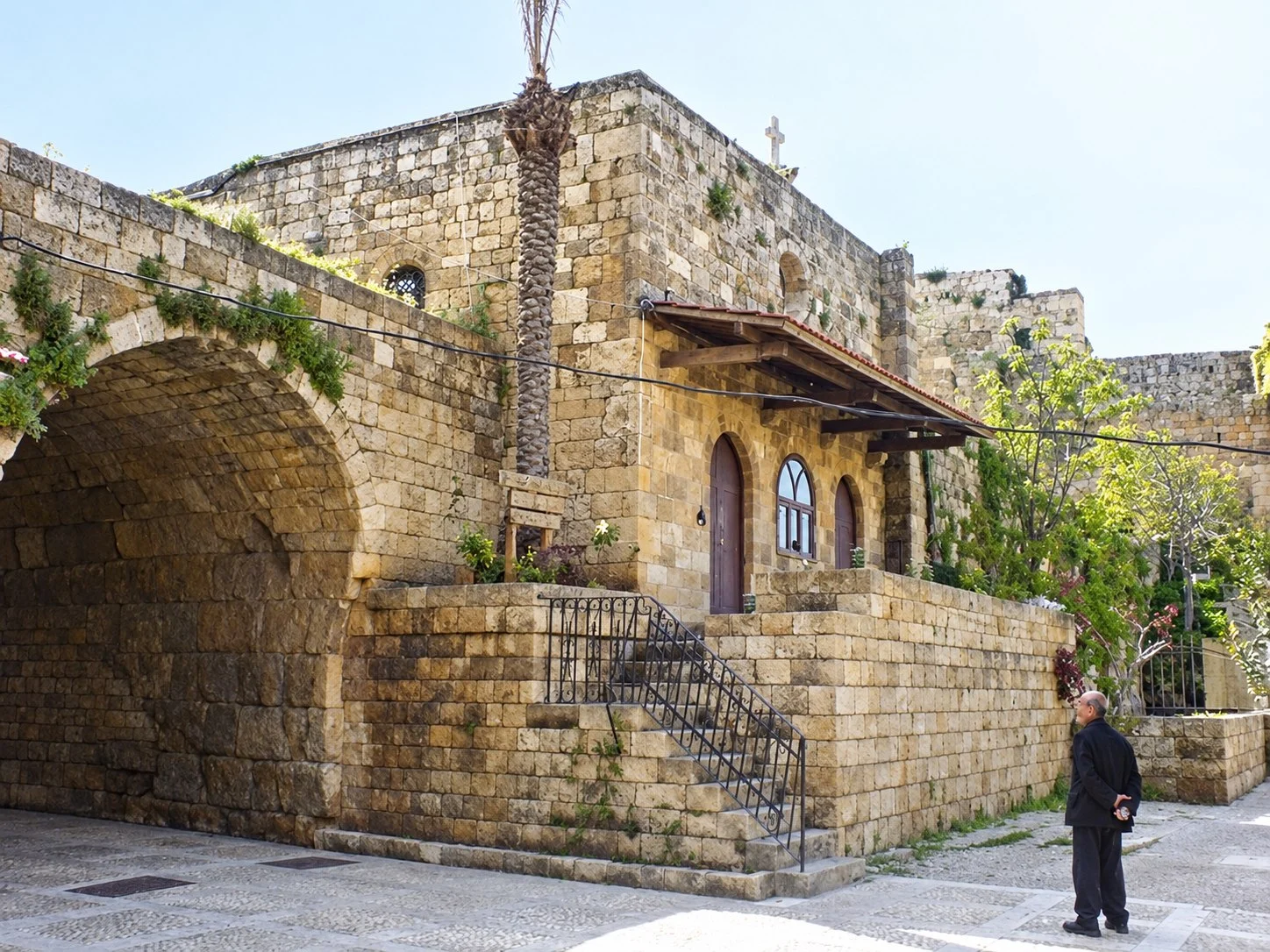 The stone church of Our Lady of the Gate beside a deep vaulted arch, its steps rising to a door under a wooden canopy