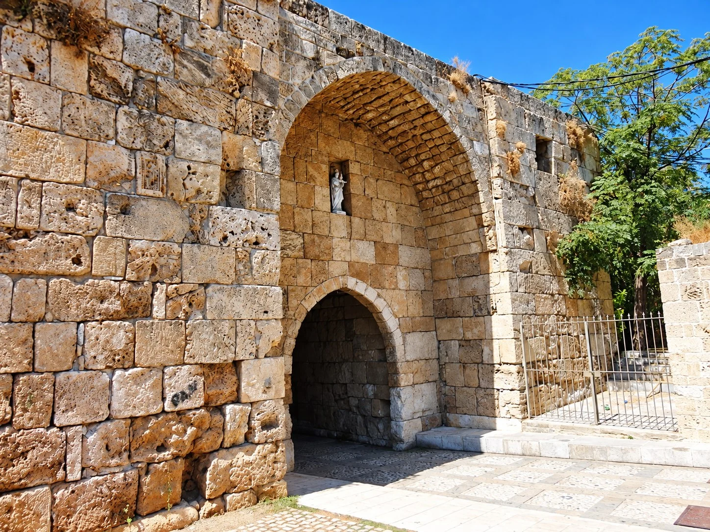 A great pointed arch in the old stone wall of Byblos, a smaller doorway beneath it and a statue of the Virgin in a niche