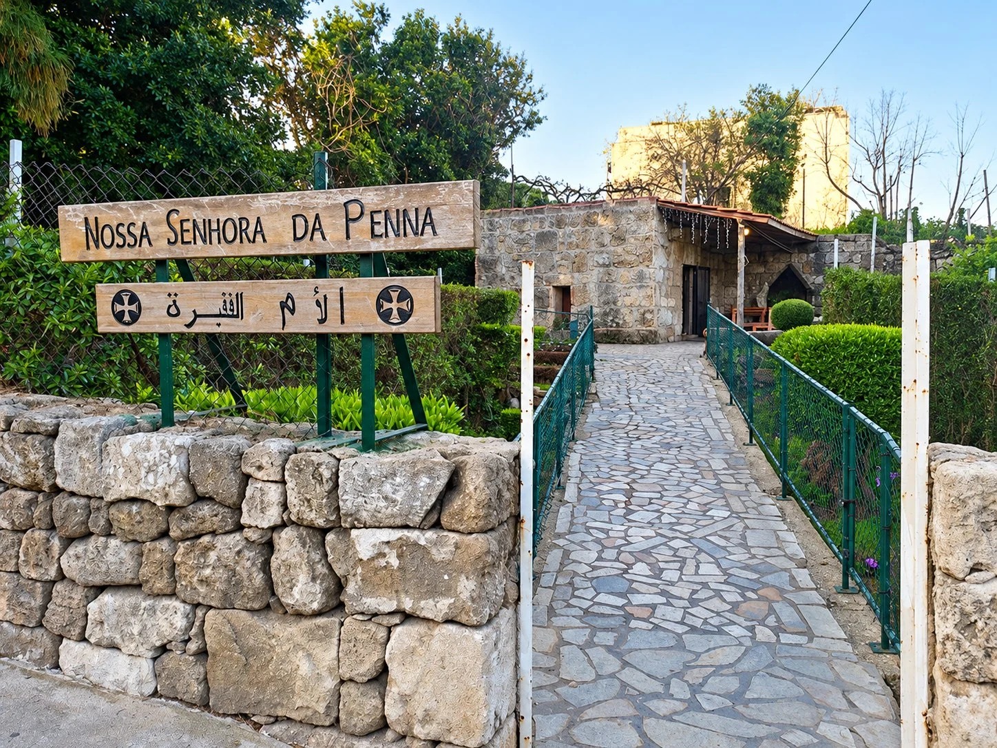 The entrance to Our Lady of Poverty: a stone wall, the wooden name boards and the paved path to the chapel